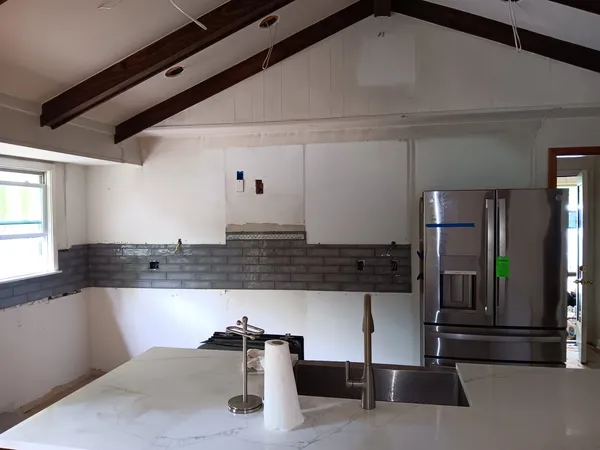 Kitchen mid-remodel with a quartz island, stainless fridge and gray subway tile going up