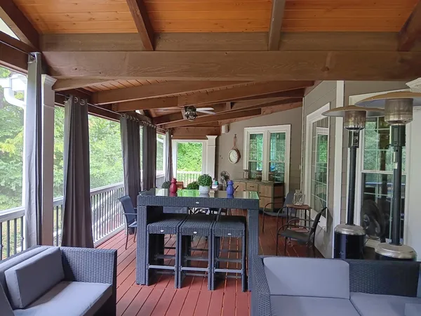 Screened porch with a timber ceiling, ceiling fans and a dining table looking out to the trees