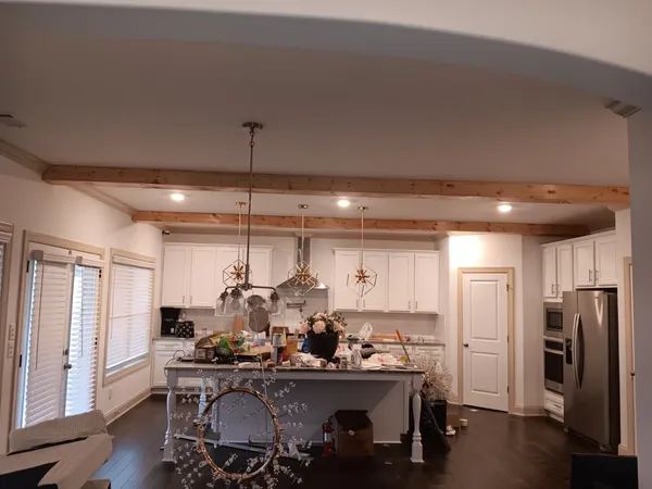White kitchen with a long island under pendant lights, exposed beams and an opening through to the living area