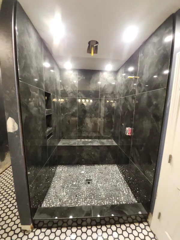 Walk-in shower lined in large dark marble-look tile with a lit niche and pebble floor