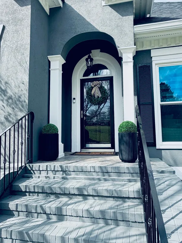 Navy-gray stucco entry with an arched head, white columns and a black front door