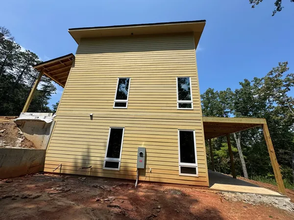 New pale yellow lap siding on a tall new-build wall with a carport framed alongside