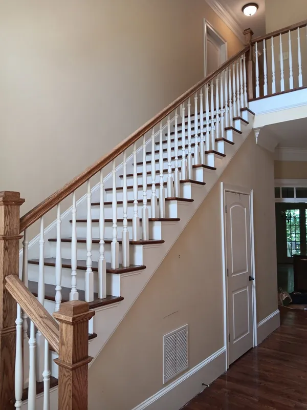 Staircase with white painted balusters and risers and a stained wood handrail