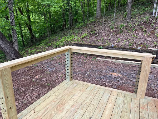 New treated deck corner with cable railing cut into a wooded hillside